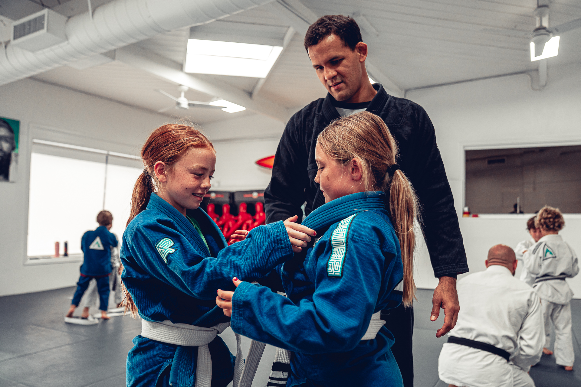 A Del Mar Jiu-Jitsu Club coach helping two children practice grips during class