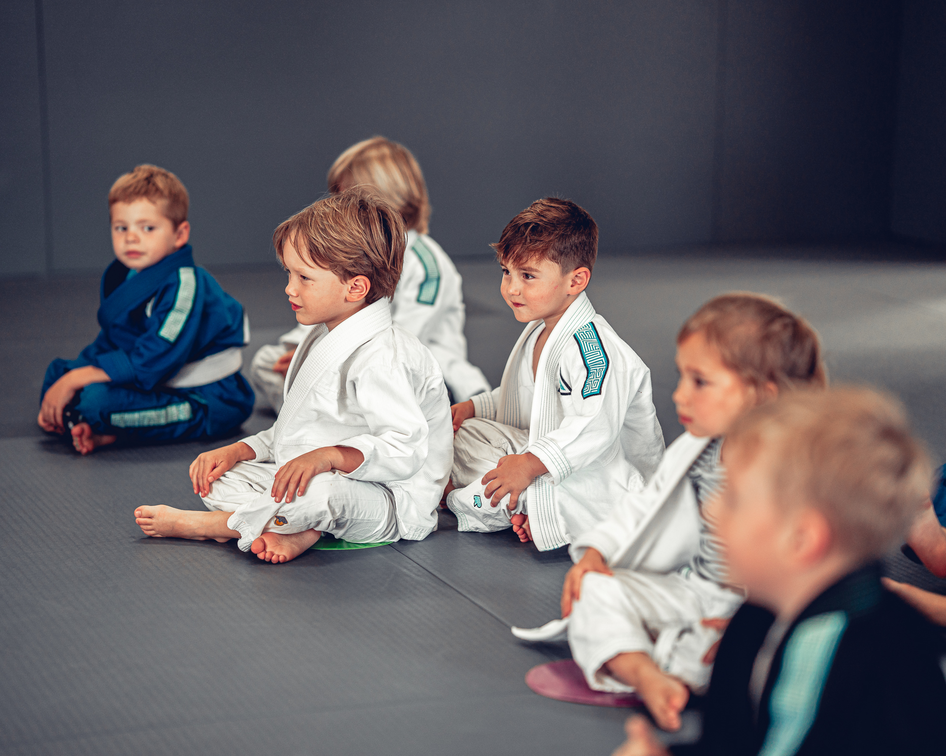Young children in Jiu-Jitsu uniforms sitting on the mat and listening to instruction